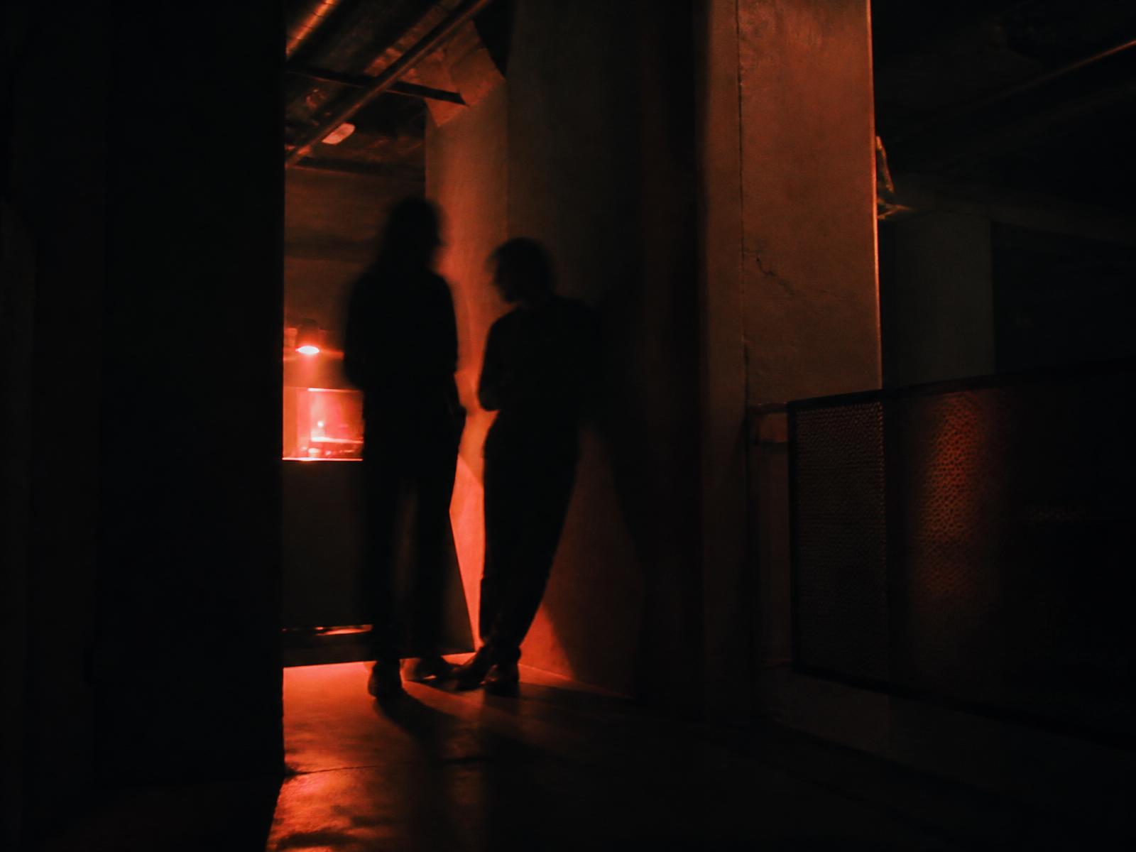 Zwei Silhouetten in einem dunklen Club, warm beleuchtet